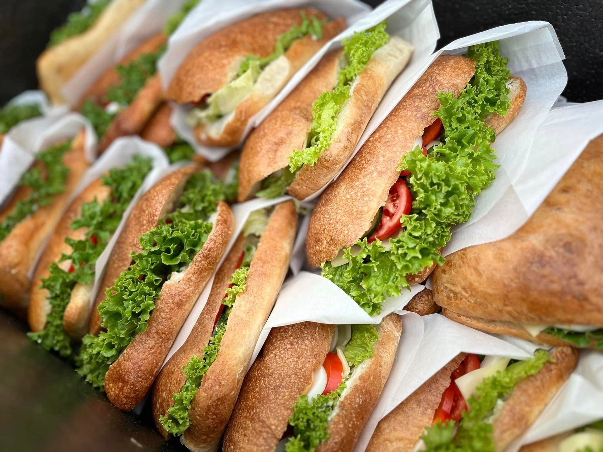 A group of sandwiches filled with lettuce and tomatoes wrapped in white paper.