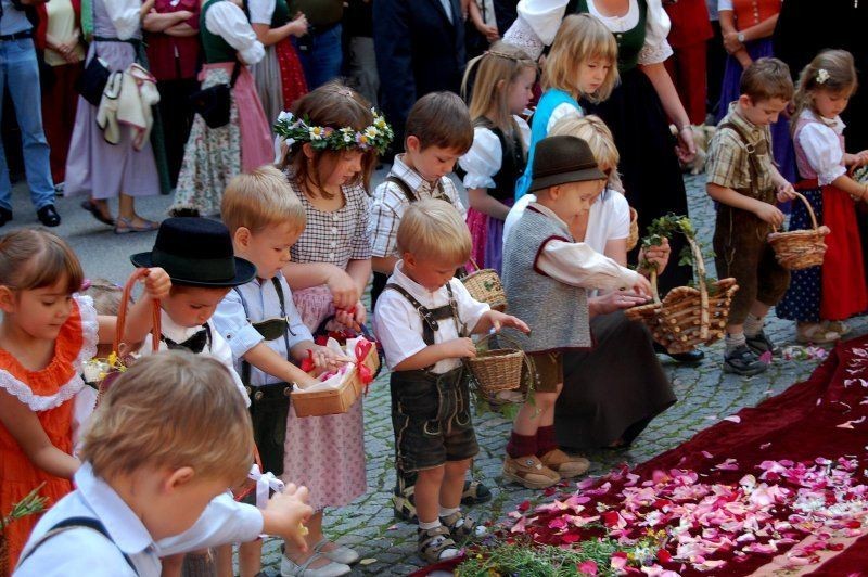 Children in traditional attire participate in a flower petal procession, holding baskets at a cultural event.
