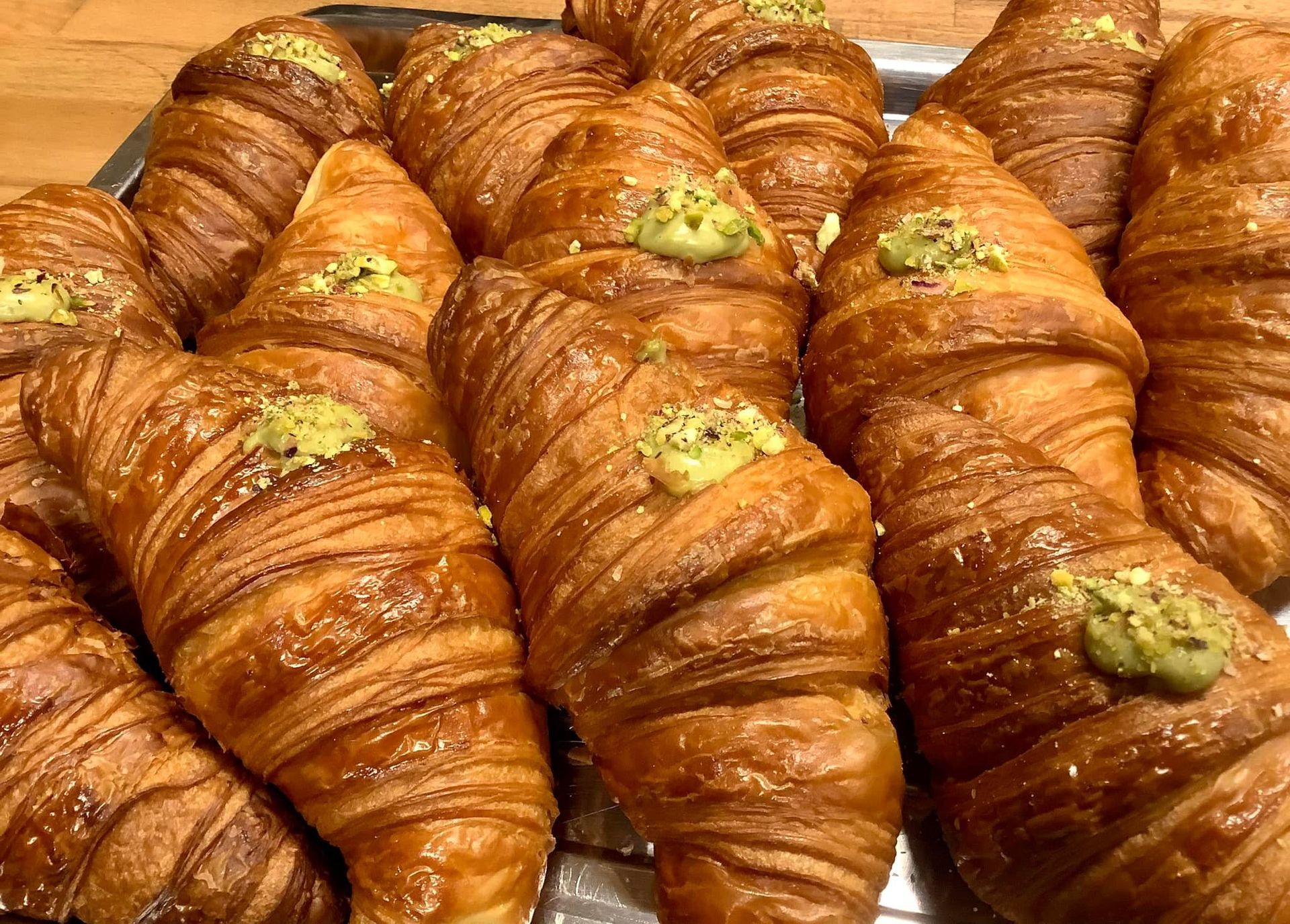 Tray of freshly baked croissants topped with a pistachio cream and nut garnish.