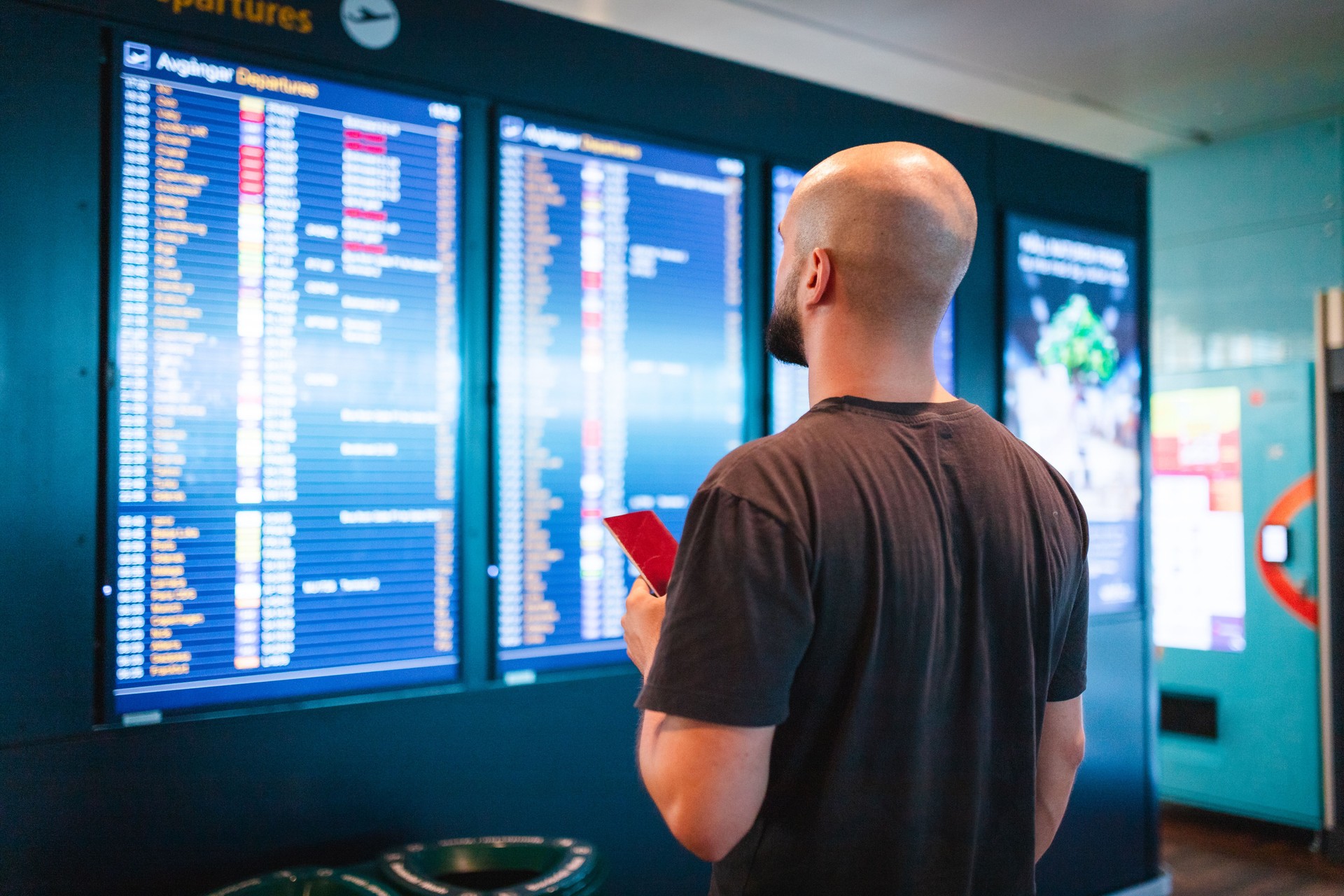 Junger Mann mit einem Reisepass und Blick auf den Flugplan am Flughafen